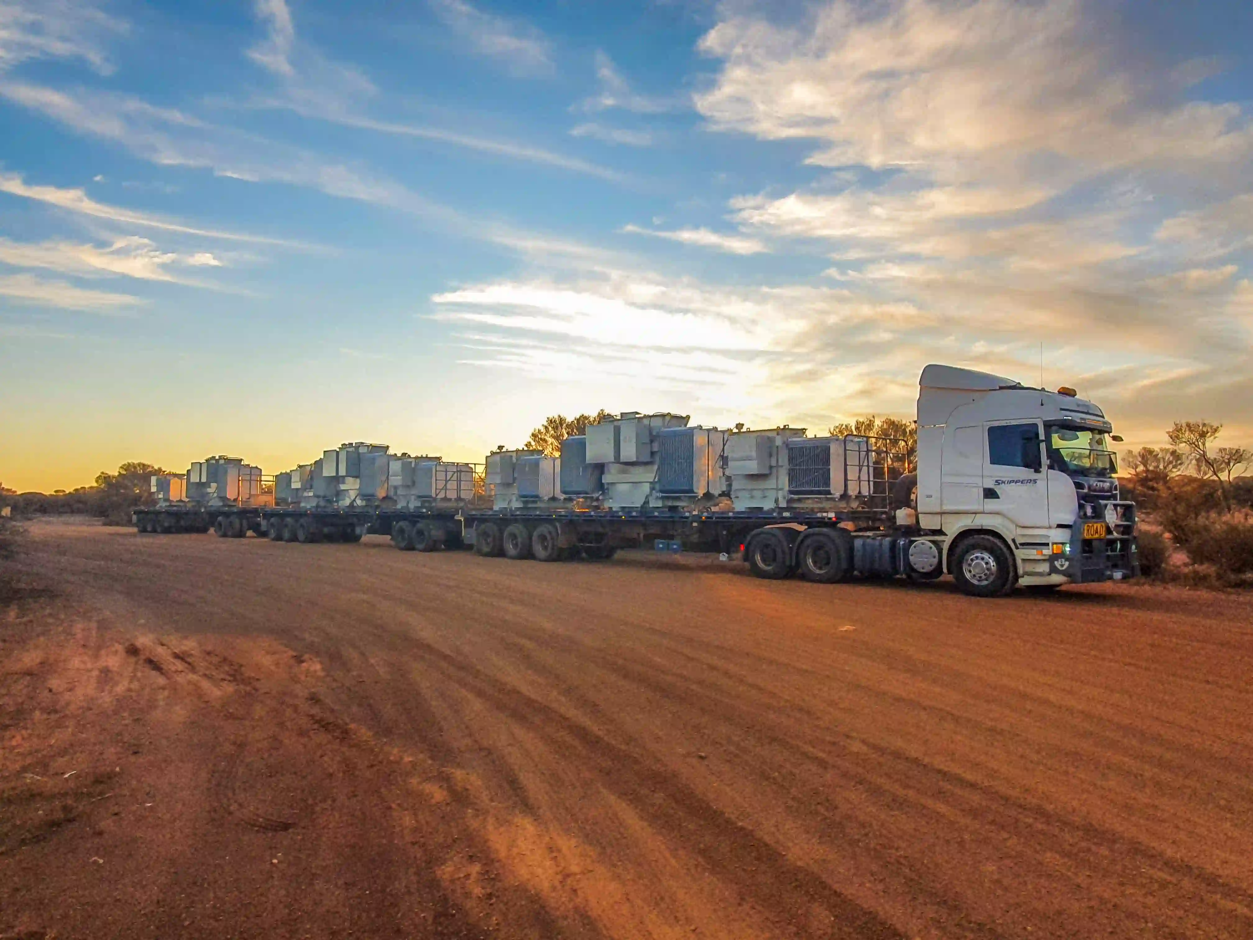 a picture of a Skippers Transport triple road train loaded with mine equipment parked on the side of the road up north in the evening as the sun sets